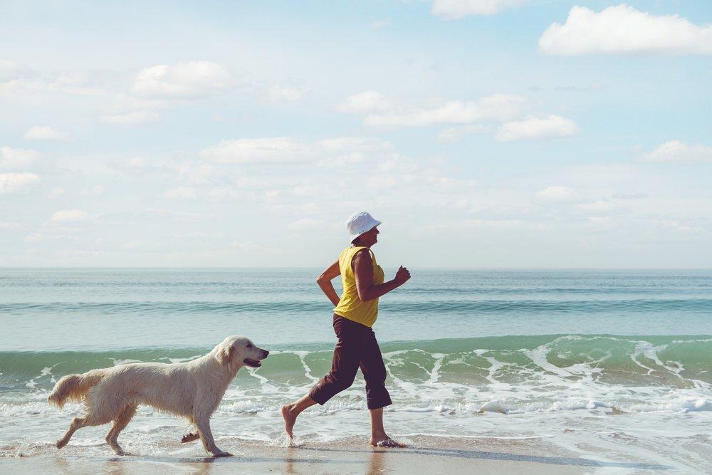 A happy person runs along the beach with a golden retriever