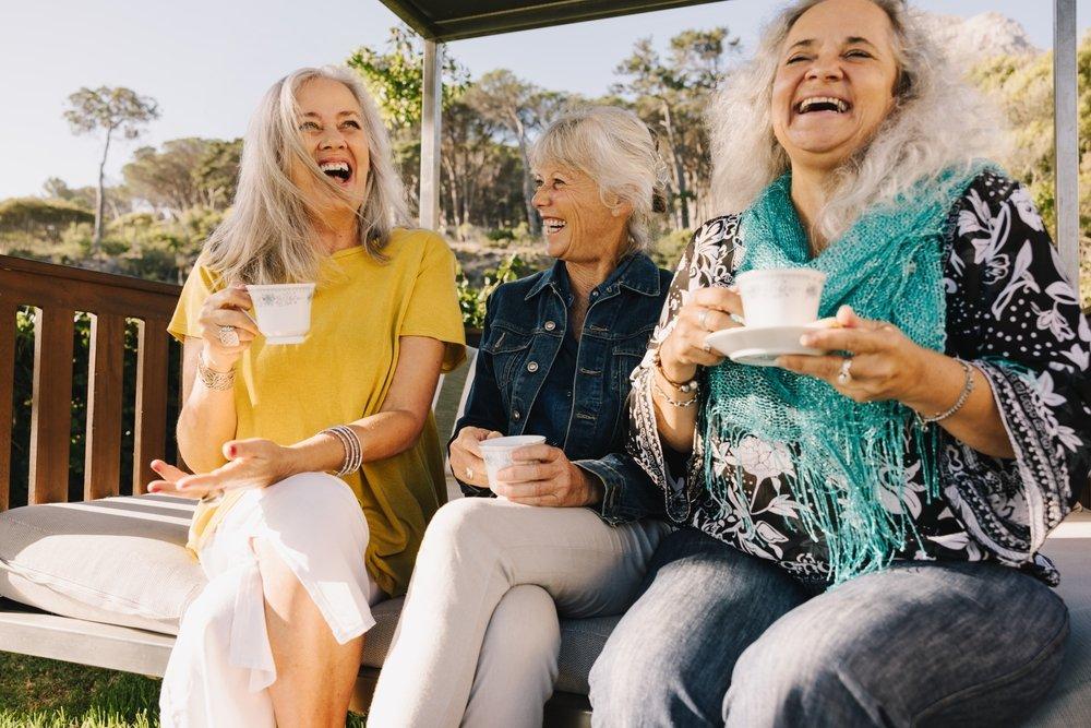 Three women talk and laugh outdoors over tea