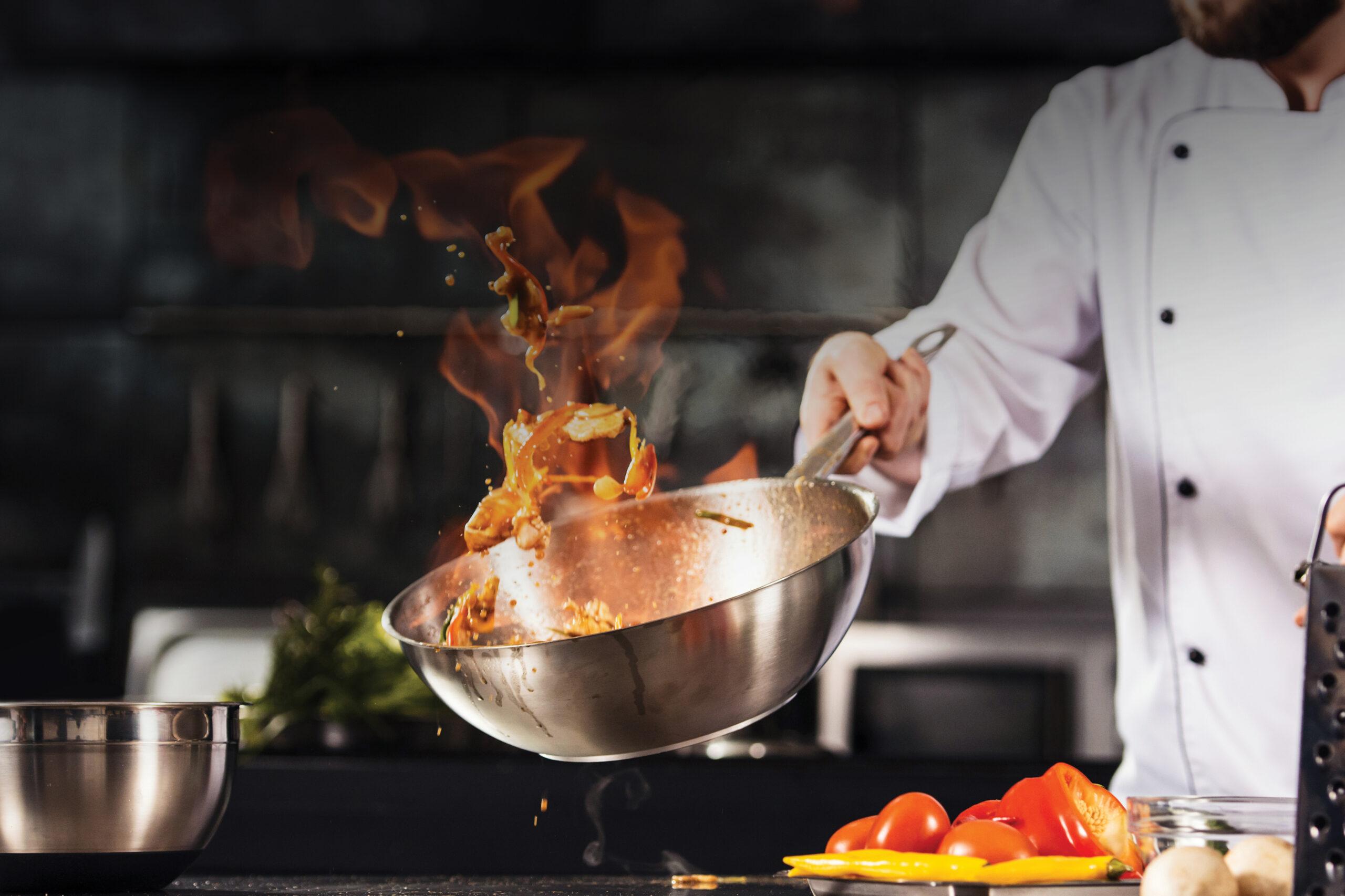 Closeup of a chef cooking with a wok — the contents are on fire