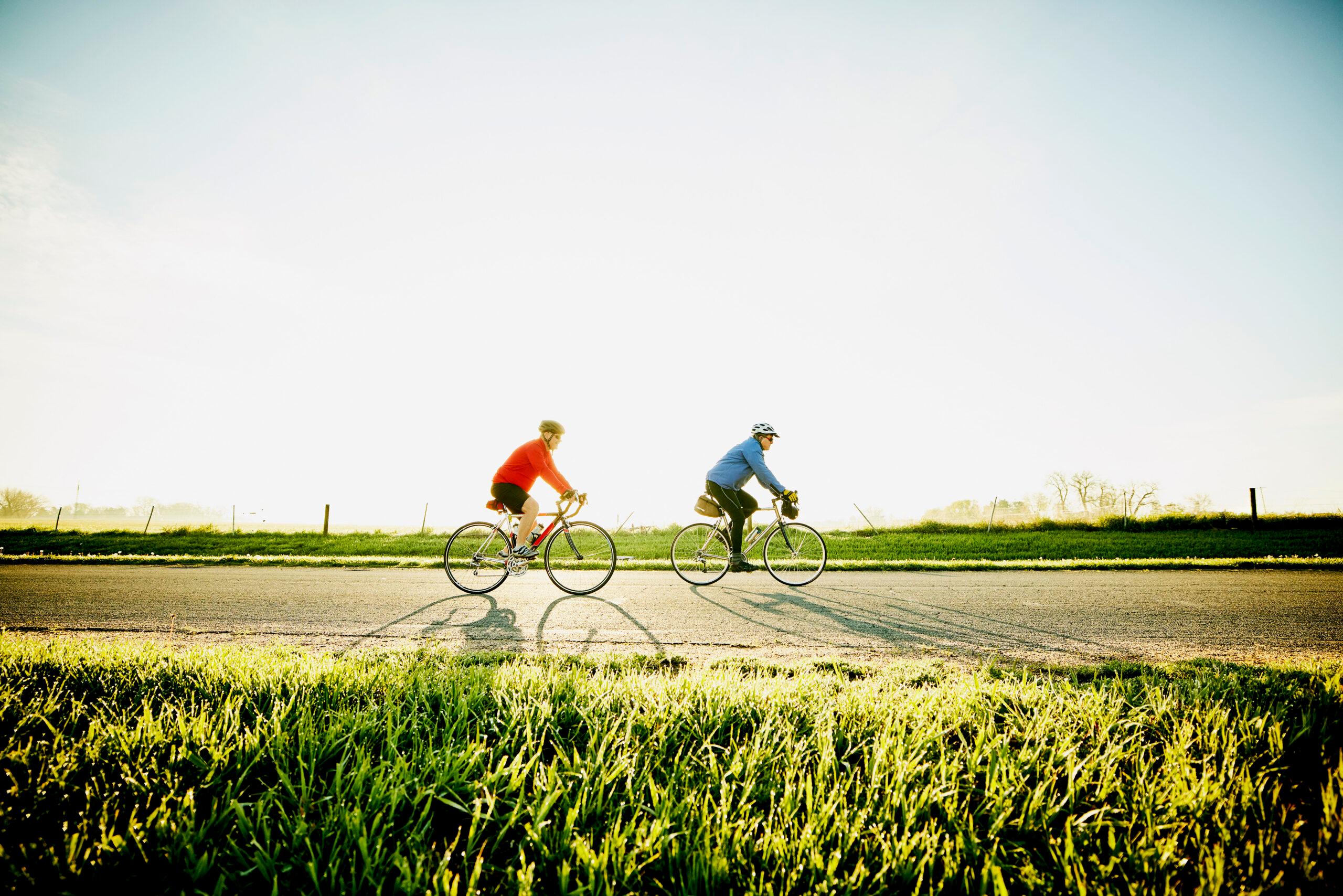 Wide shot of senior male friends on sunrise bike ride on rural road