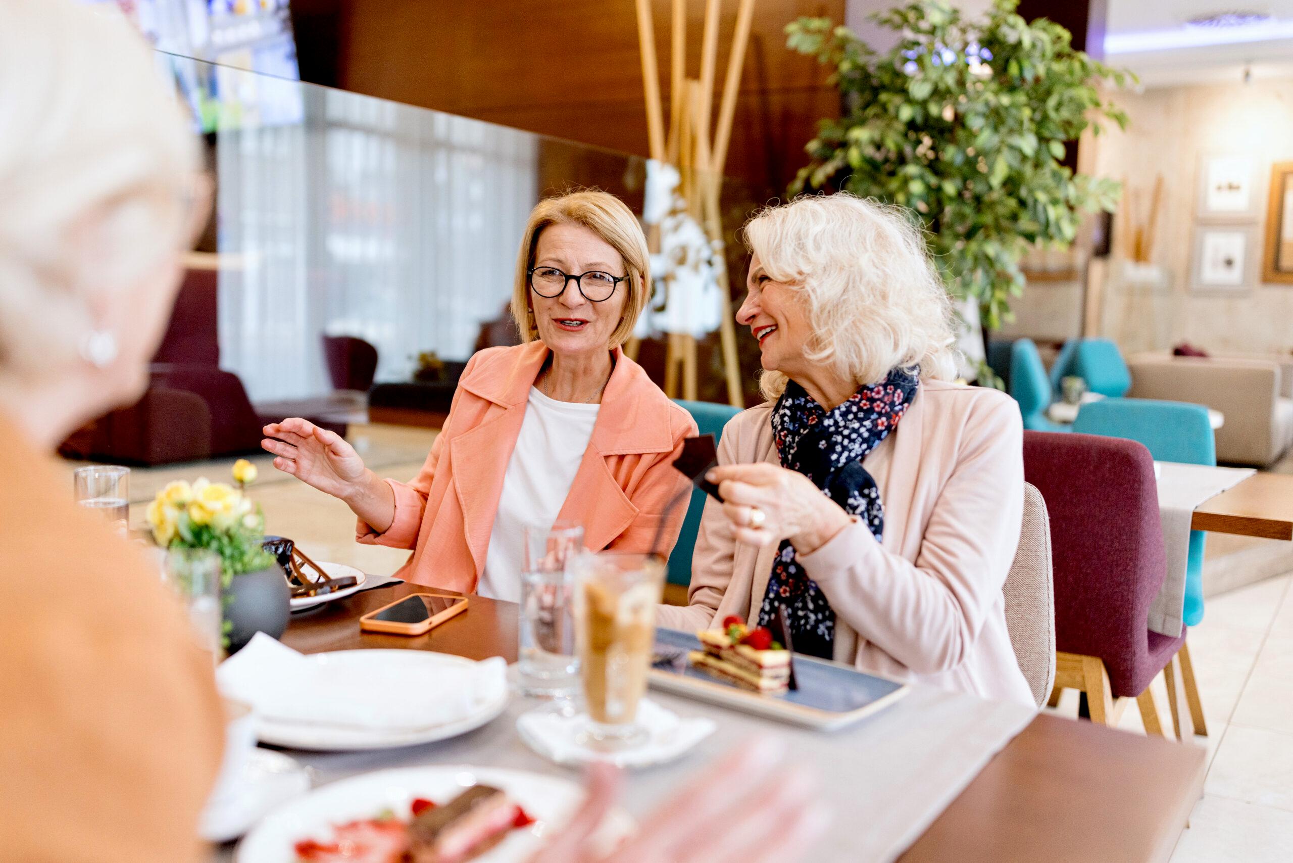 Senior female friends on vacation eating cake in a hotel